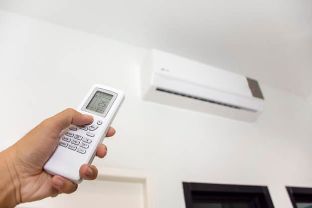 Human hand is using white remote of air conditioner for turn on and adjust air conditioner in a room