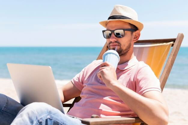 Man having a drink at the beach and working on laptop