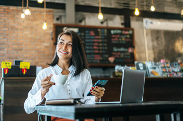 Woman sitting happily working with a smartphone in a coffee shop and notebook
